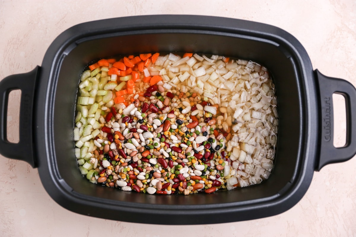 Beans, oil, onion, garlic, carrots and celery added to a slow cooker.