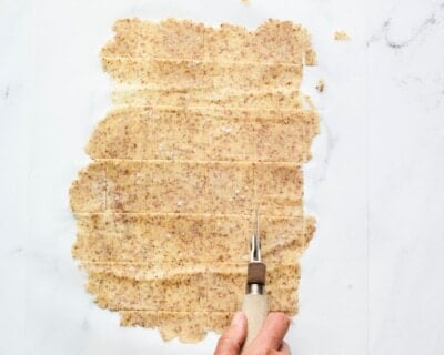 Pizza cutter slicing dough into squares for almond flour crackers.