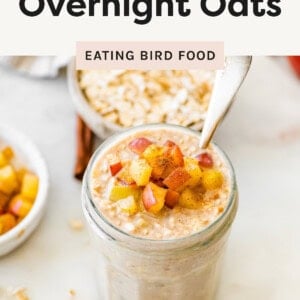 A jar of apple cinnamon overnight oats topped with diced apples and cinnamon, with a spoon inside the jar.