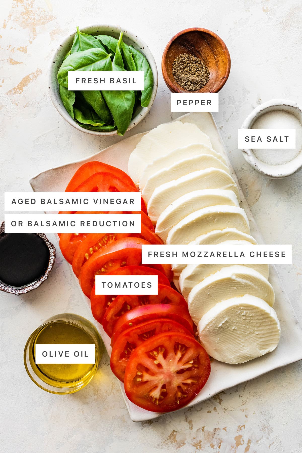 Ingredients measured out to make Easy Caprese Salad: fresh basil, pepper, sea salt, balsamic vinegar, fresh mozzarella, tomatoes and olive oil.