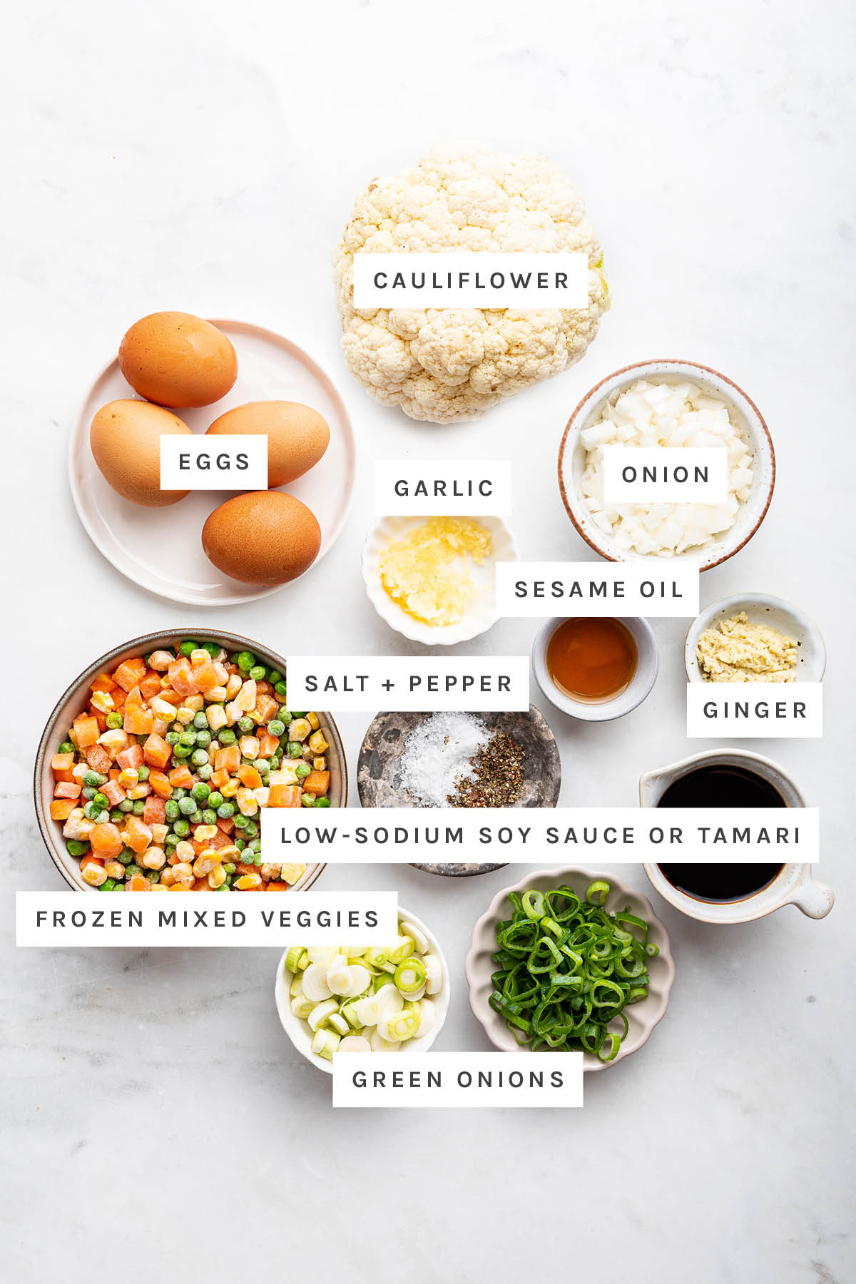 Ingredients measured out to make Cauliflower Fried Rice: eggs, cauliflower, garlic, onion, sesame oil, ginger, salt, pepper, soy sauce, frozen mixed veggies and green onions.