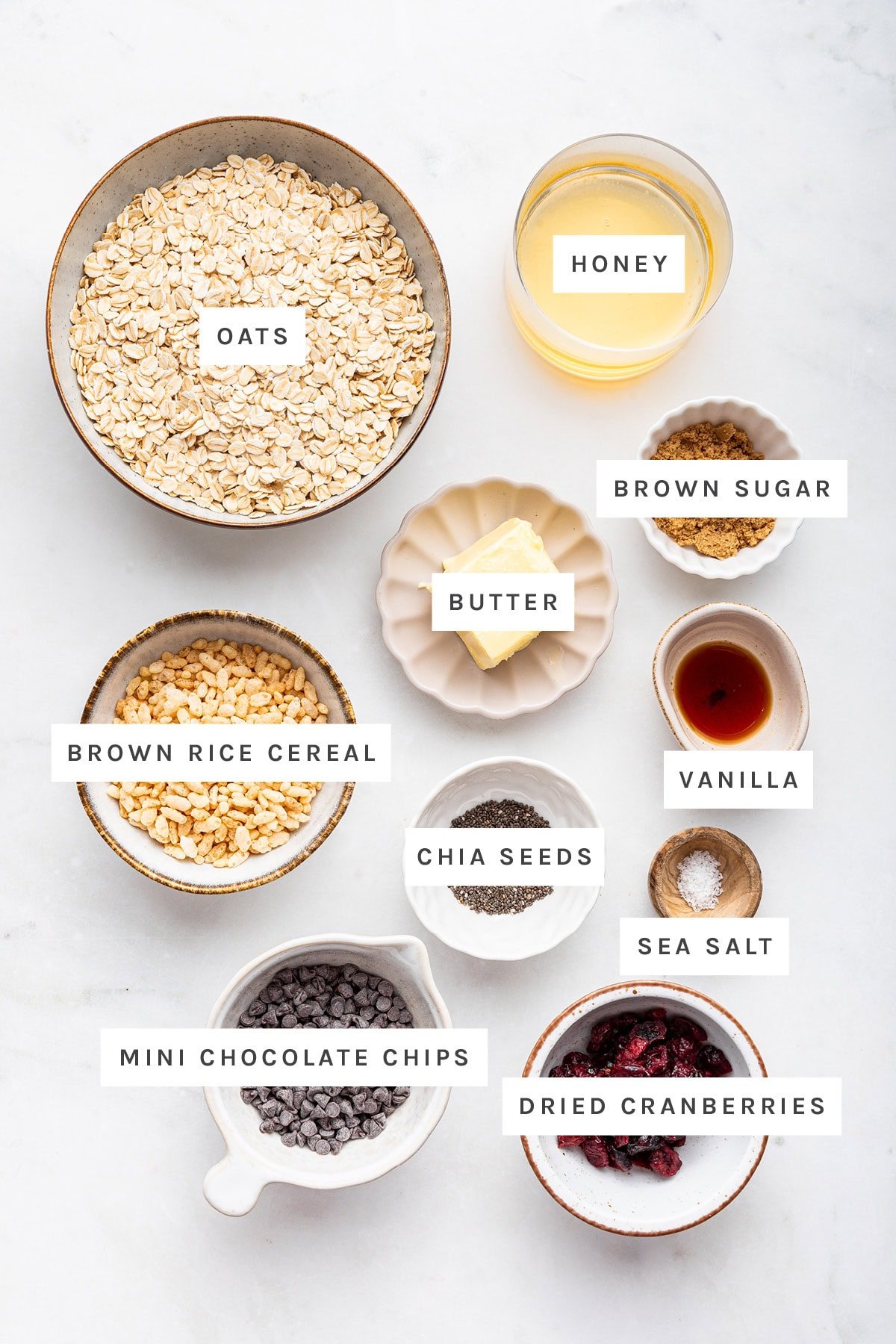 Ingredients measured out to make Chewy Granola Bars: oats, honey, butter, brown sugar, brown rice cereal, chia seeds, vanilla, sea salt, mini chocolate chips and dried cranberries.