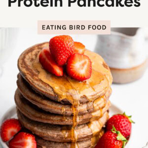 Stack of fluffy chocolate protein pancakes topped with peanut butter and fresh strawberries on a white plate.