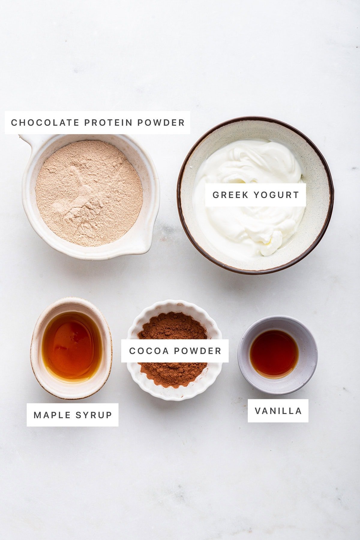 Ingredients measured out to make Chocolate Protein Pudding: chocolate protein powder, Greek yogurt, maple syrup, cocoa powder and vanilla.