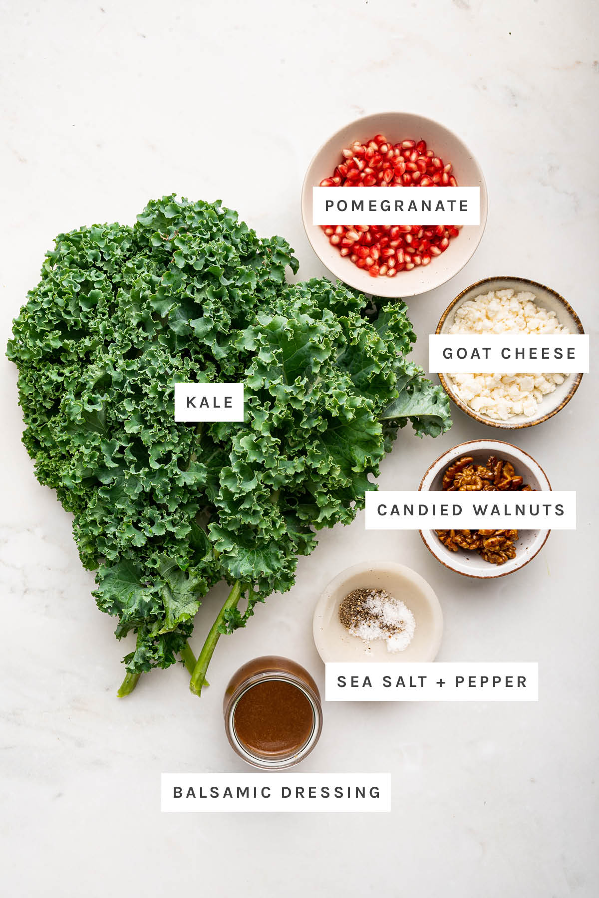 Ingredients measured out to make Christmas Salad: kale, pomegranate, goat cheese, candied walnuts, sea salt, pepper and balsamic dressing.