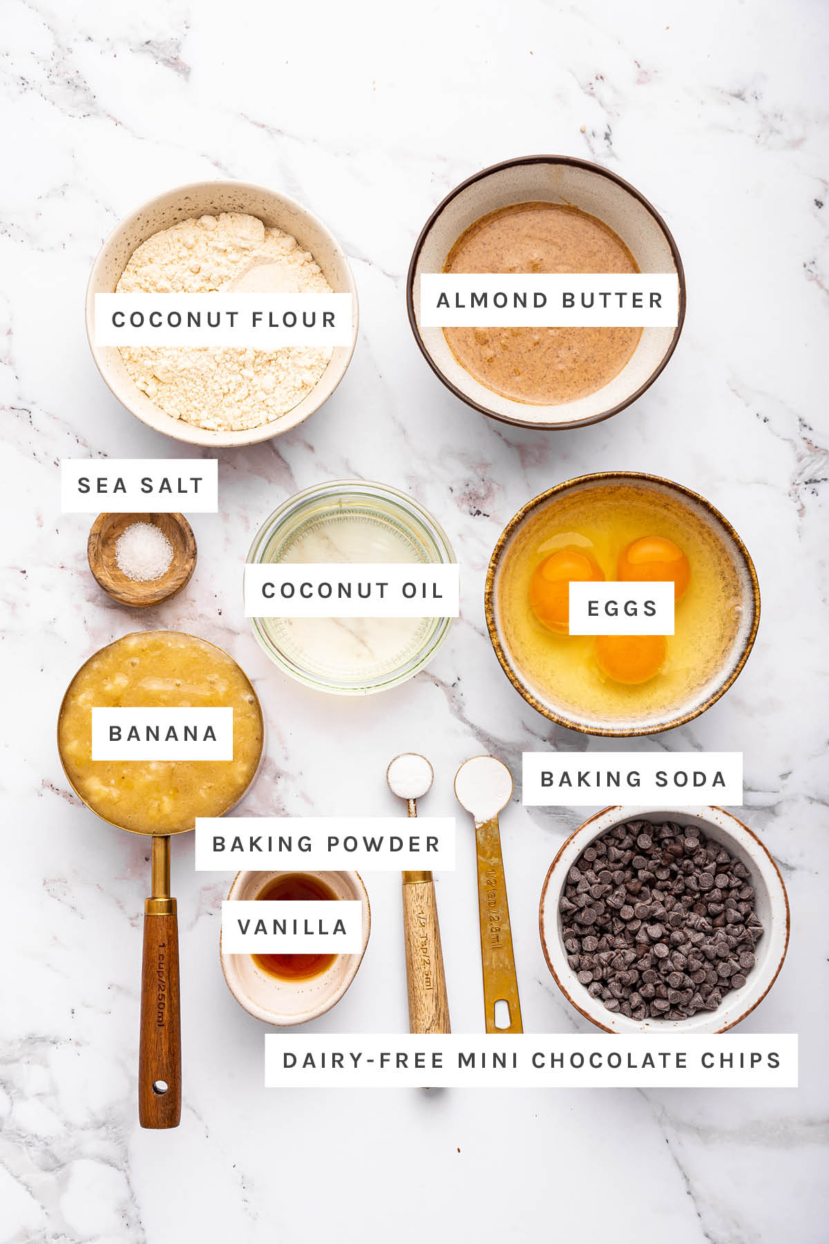 Ingredients measured out to make Coconut Flour Banana Bread: coconut flour, almond butter, sea salt, coconut oil, eggs, banana, baking powder, baking soda, vanilla and dairy-free mini chocolate chips.