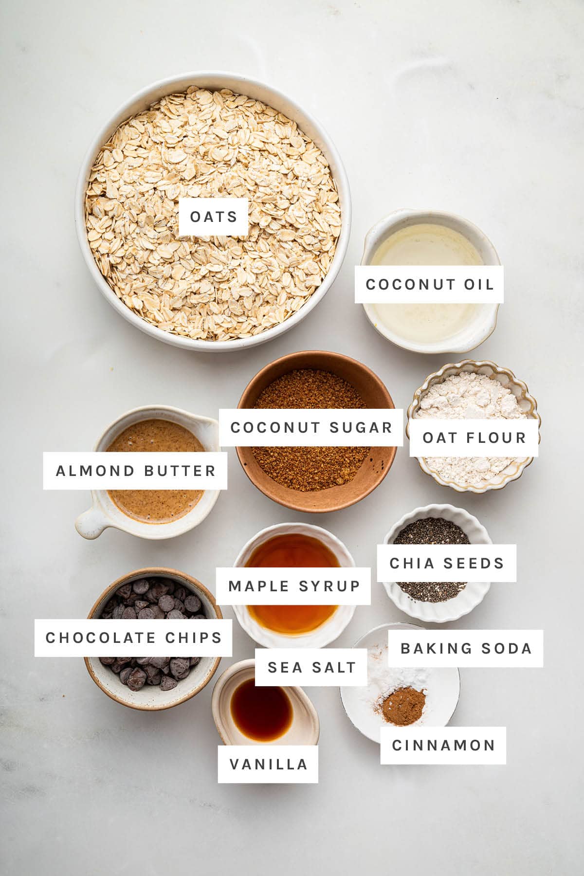 Ingredients measured out to make Chocolate Chip Cookie Granola: oats, coconut oil, coconut sugar, oat flour, almond butter, maple syrup, chia seeds, chocolate chips, sea salt, baking soda, cinnamon and vanilla.