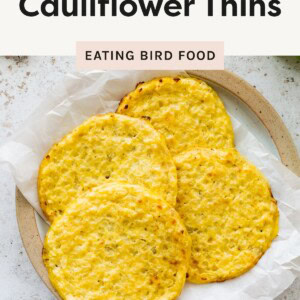 Four golden cottage cheese cauliflower thins on a plate lined with parchment paper.