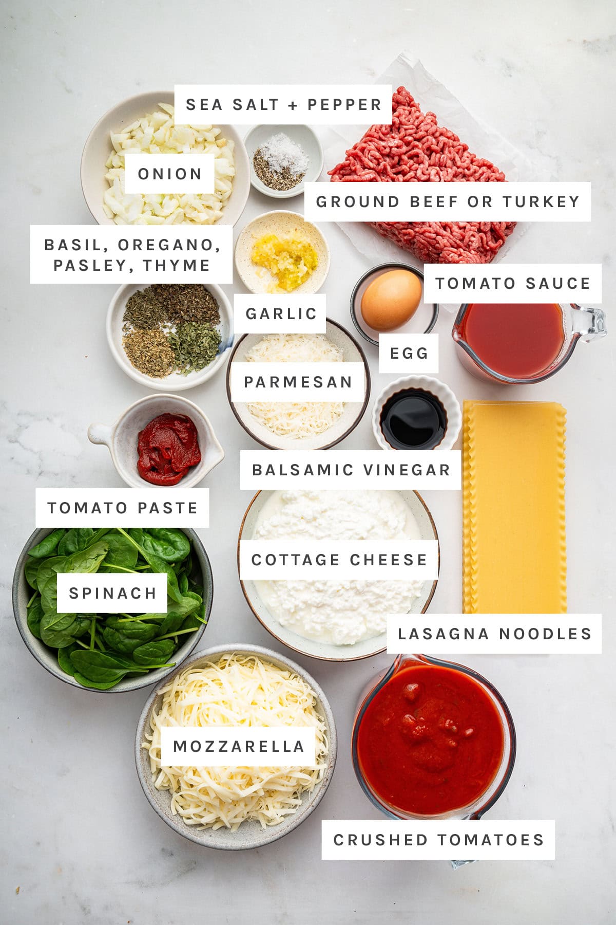 Ingredients measured out to make Healthy Lasagna: sea salt, pepper, onion, ground beef, garlic, basil, oregano, parsley, thyme, tomato sauce, parmesan, egg, tomato paste, balsamic vinegar, cottage cheese, lasagna noodles, spinach, mozzarella and crushed tomatoes.