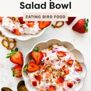 Two bowls of high-protein strawberry pretzel salad topped with fresh strawberries and crushed pretzels, surrounded by whole strawberries and gold spoons.