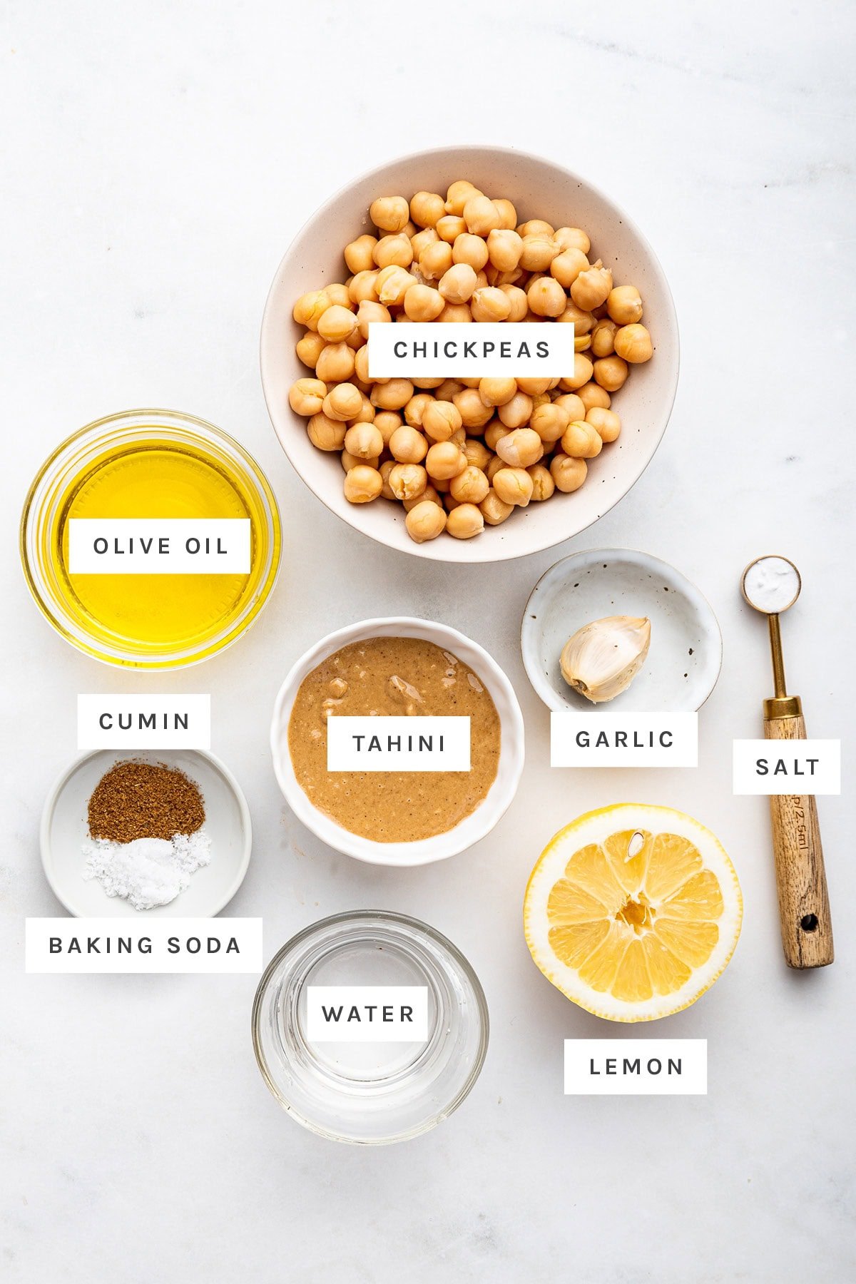 Ingredients measured out to make hummus: olive oil, chickpeas, garlic, tahini, lemon, cumin, baking soda and salt.