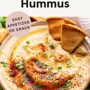 Bowl of hummus garnished with paprika, parsley, olive oil and pita.