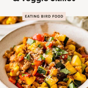 Bowl of Italian ground turkey and veggie skillet topped with parmesan and fresh basil, featuring colorful zucchini, squash, and bell peppers.