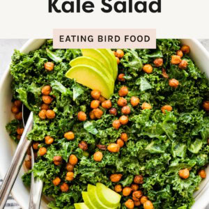 Bowl of massaged kale salad topped with roasted chickpeas and sliced avocado.