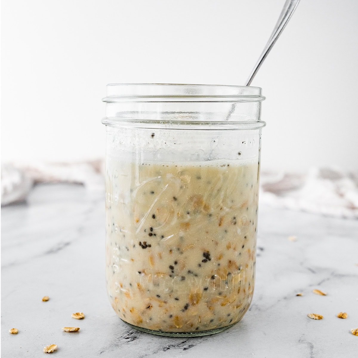 Ingredients for overnight oats combined in a mason jar with a spoon in the jar as well.