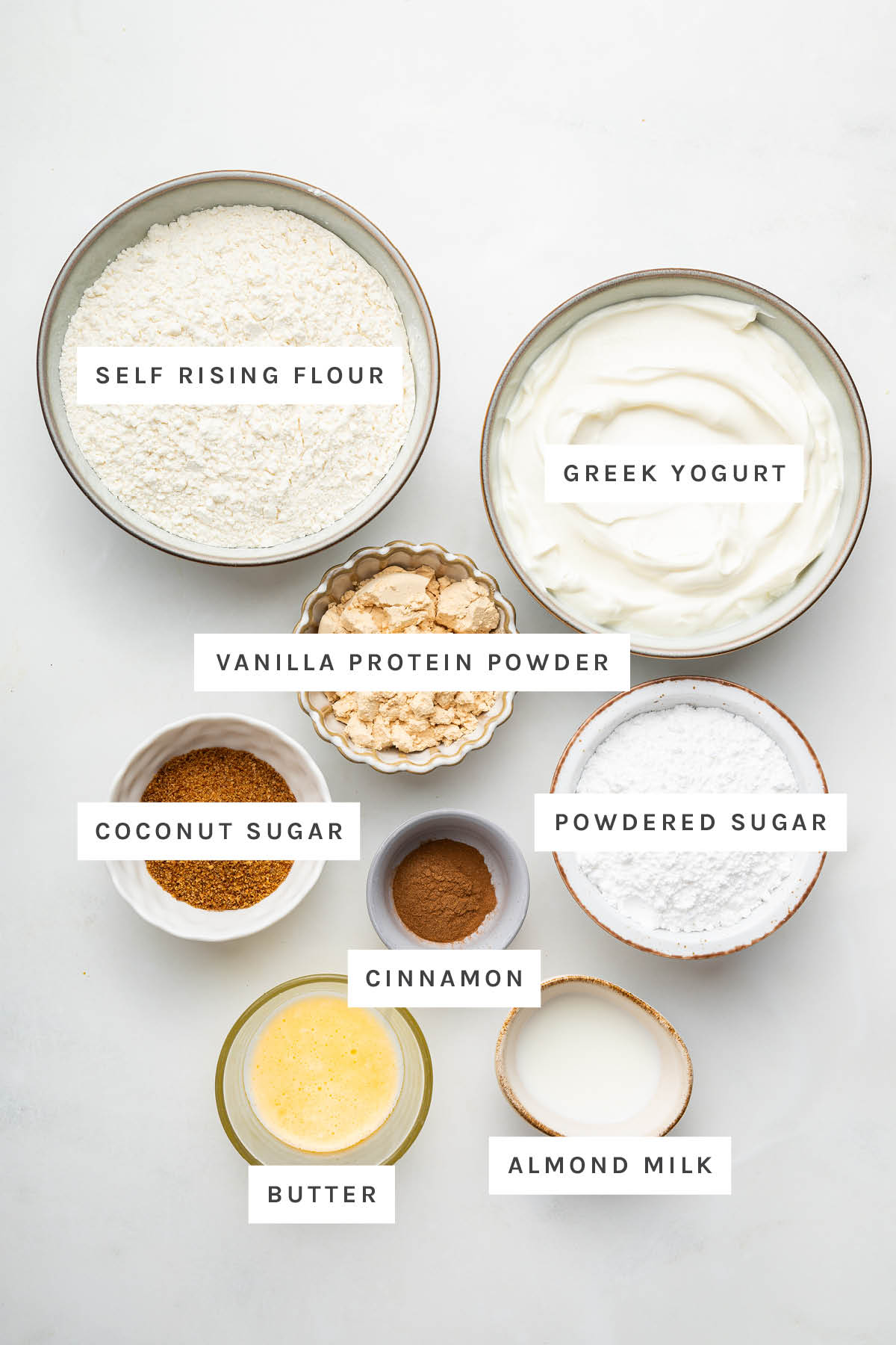 Ingredients measured out to make Protein Cinnamon Rolls: self rising flour, Greek yogurt, vanilla protein powder, powdered sugar, coconut sugar, cinnamon, butter and almond milk.