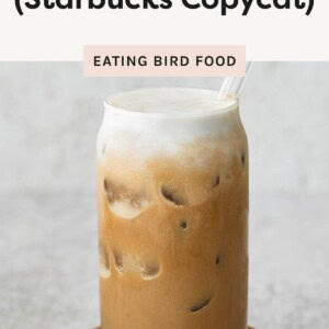 Glass of iced coffee topped with protein cold foam and a clear straw, sitting on a small wooden coaster.