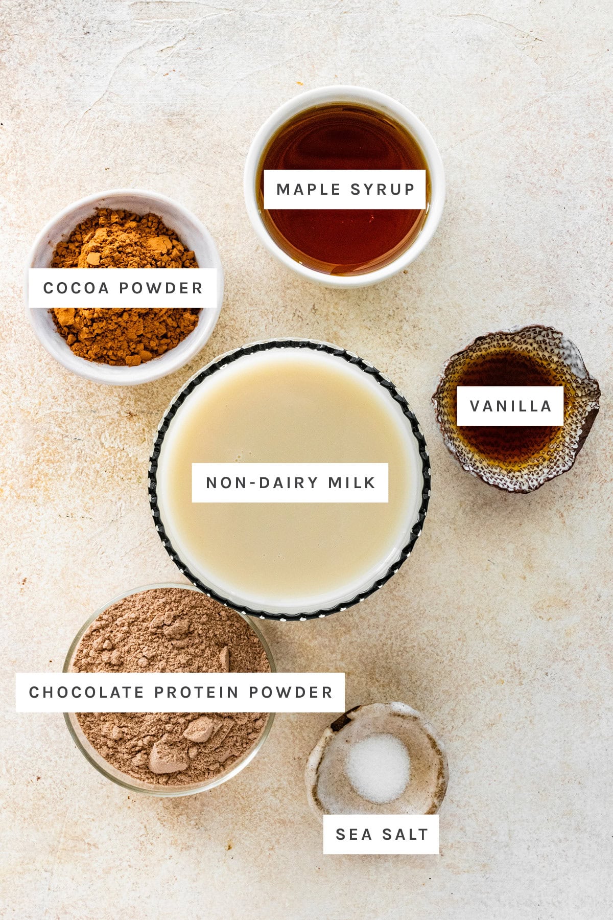Ingredients measured out to make Protein Hot Chocolate: cocoa powder, maple syrup, vanilla, oat milk, chocolate protein powder and sea salt.