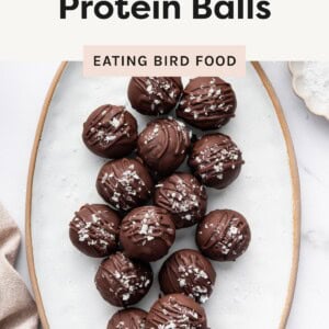 Overhead view of salted chocolate protein balls arranged on a white plate, topped with flaky sea salt and chocolate drizzle.