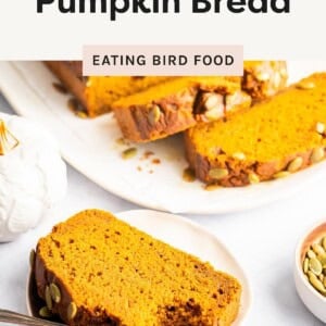 Slice of pumpkin bread with pepitas on a plate, with more slices on a serving dish in the background.