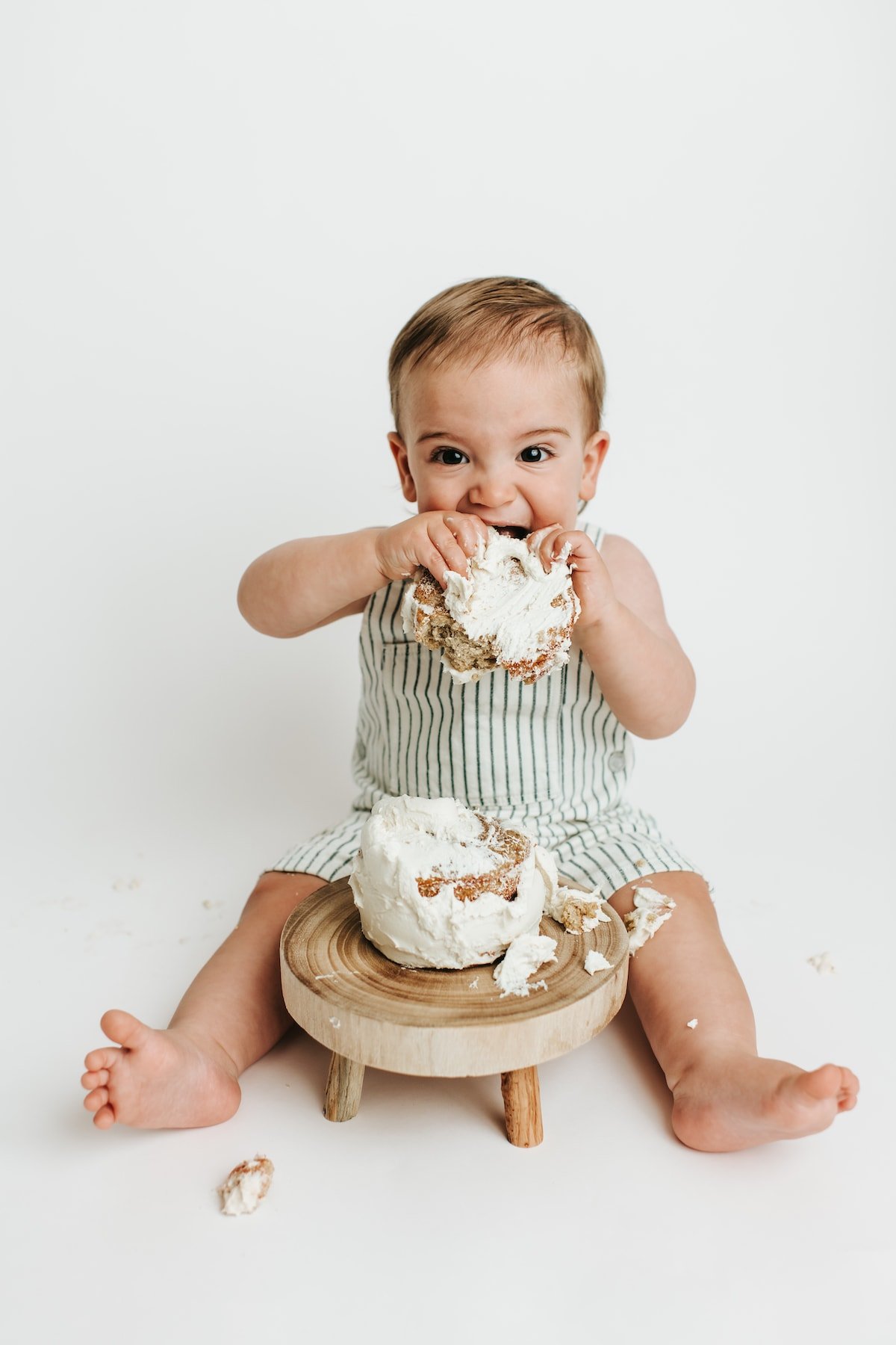 Baby boy with a smash cake, putting a large piece of the cake in his mouth.