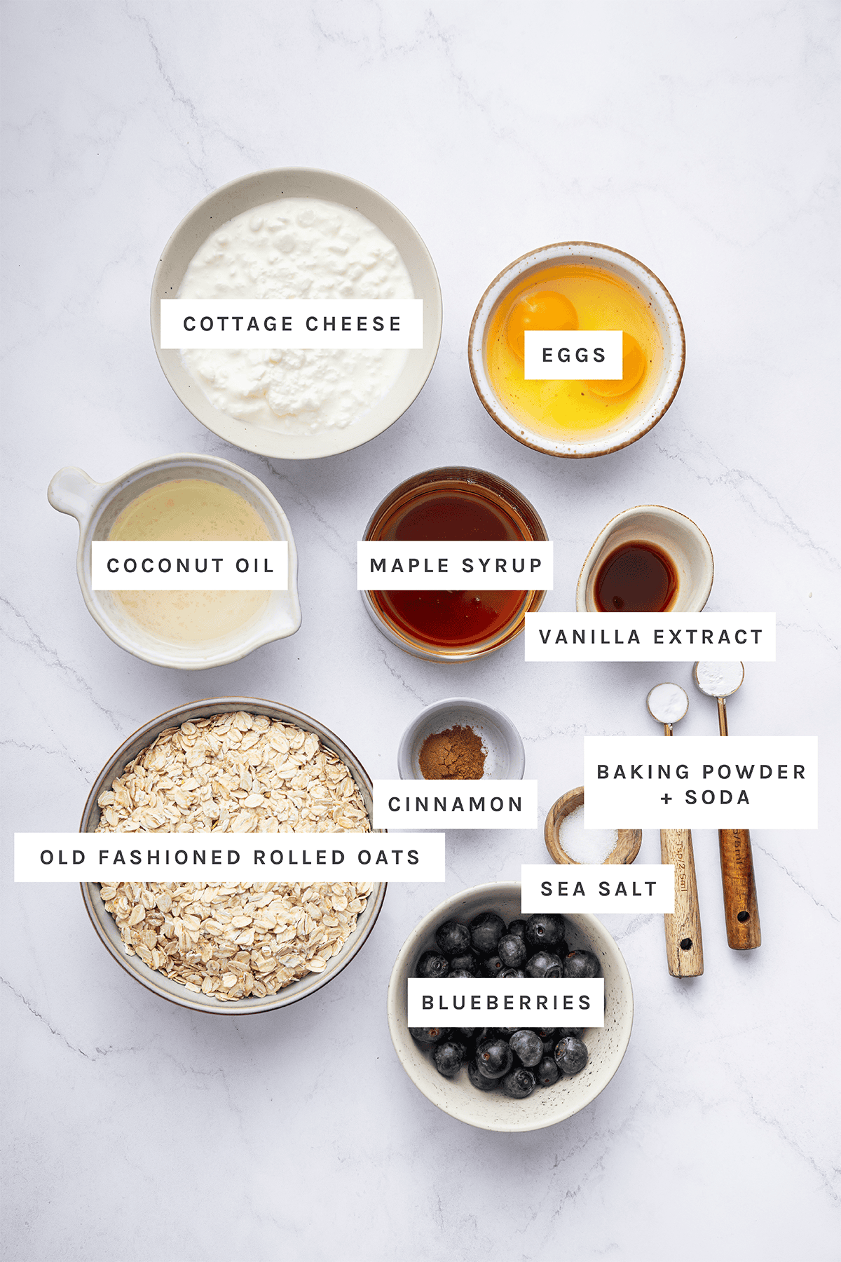 Ingredients measured out to make Cottage Cheese Muffins: Cottage cheese, eggs, coconut oil, maple syrup, vanilla extract, old fashioned rolled oats, cinnamon, baking powder, baking soda, sea salt, blueberries.