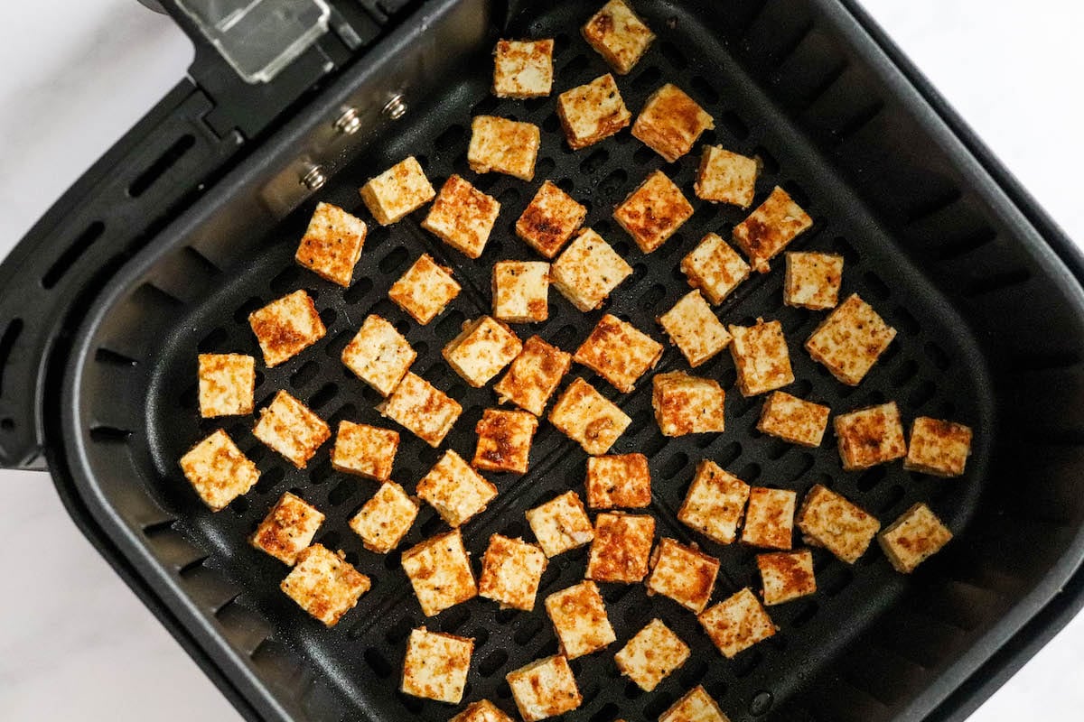Cubes of seasoned tofu in an air fryer basket.