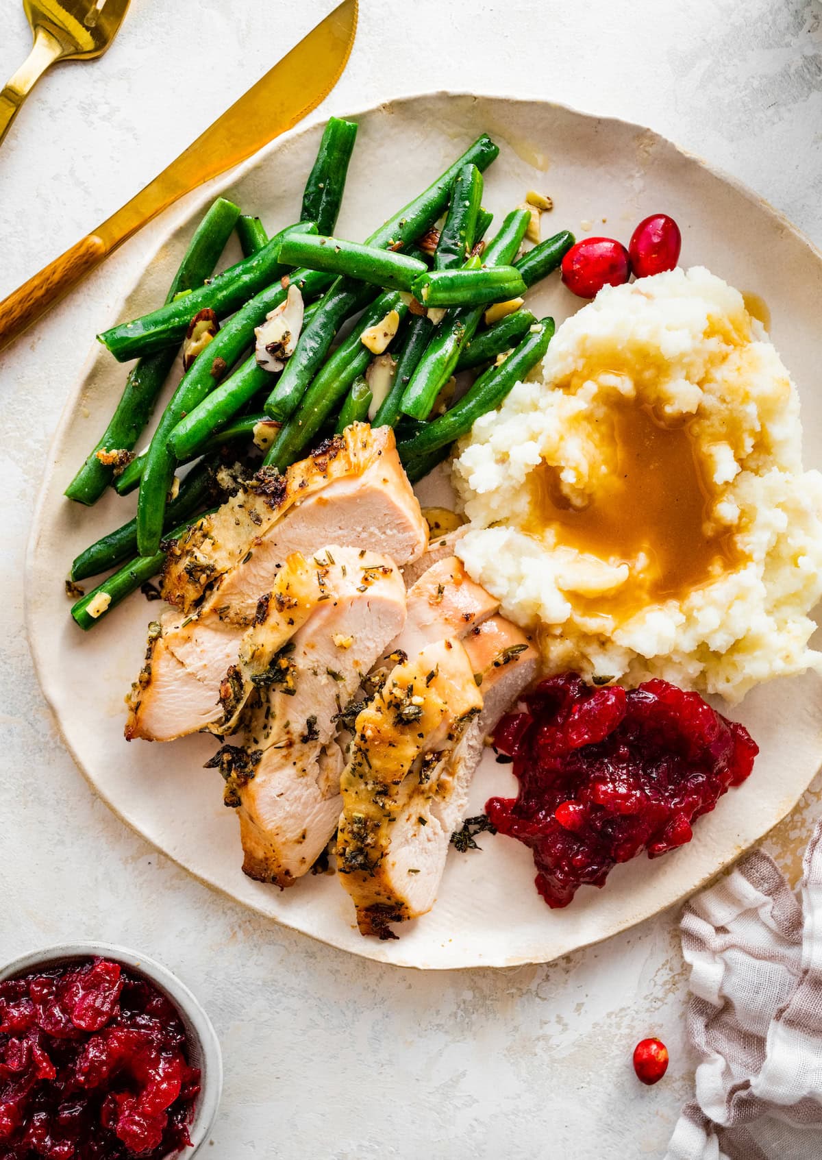 Slices of an air fryer turkey breast served on a white plate alongside green beans, mashed potatoes and gravy and cranberry sauce.