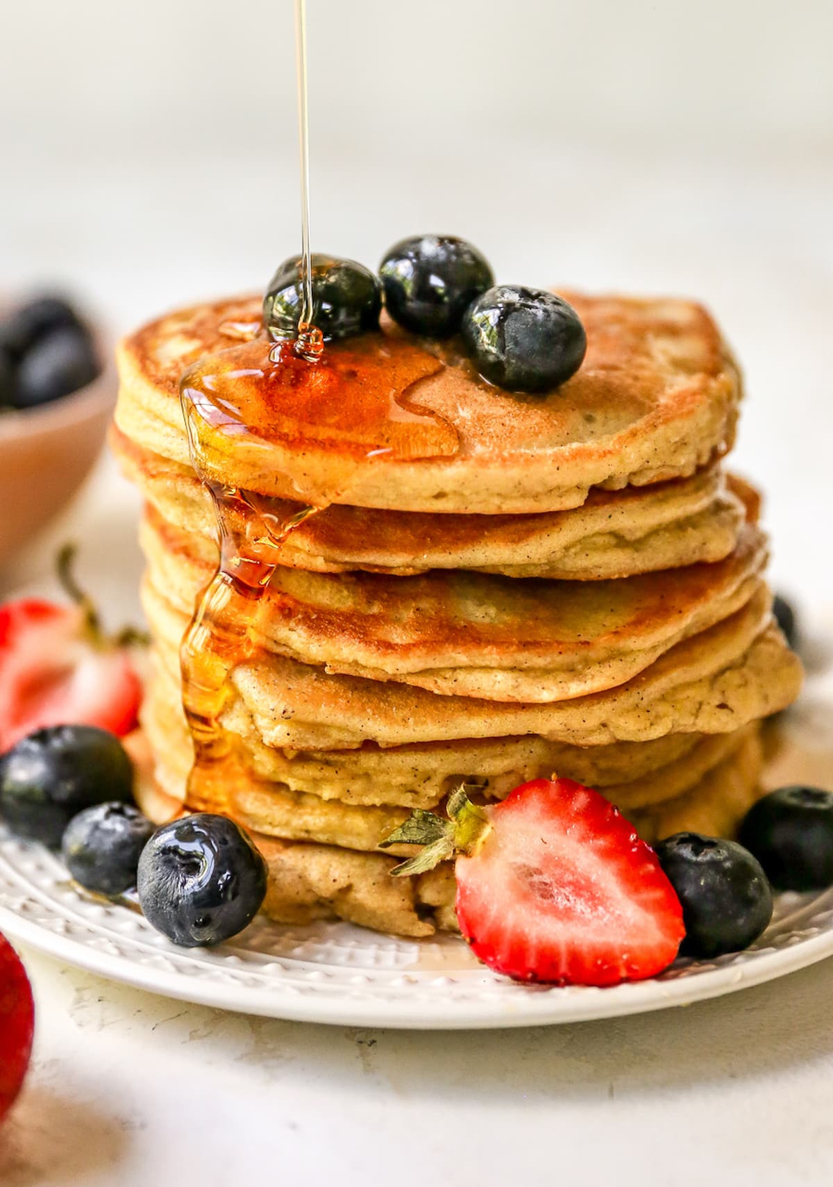 Stack of almond flour pancakes served with berries and maple syrup being drizzled on.