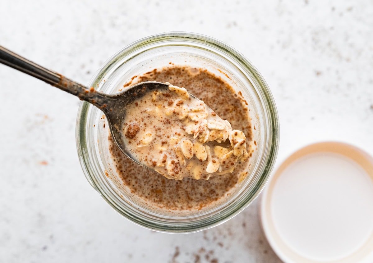 A spoon scooping creamy apple cinnamon overnight oats from a glass jar.