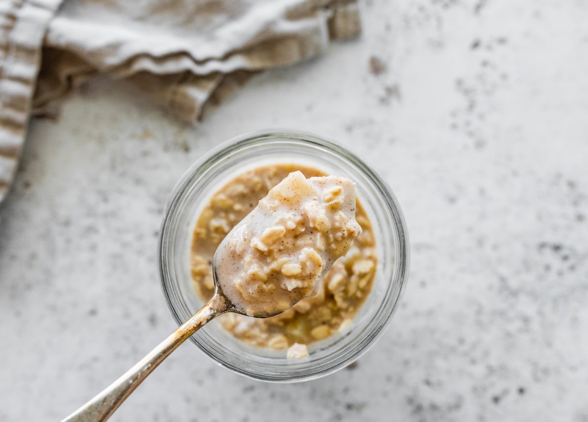 A spoonful of apple cinnamon overnight oats lifted from a jar, showing oats and creamy texture.