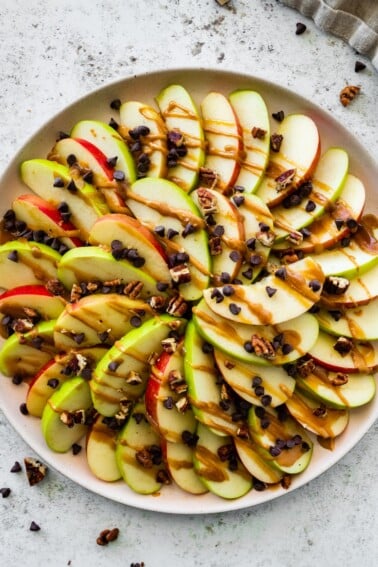 A large plate of apple nachos topped with a date caramel drizzle, mini chocolate chips, and pecans.