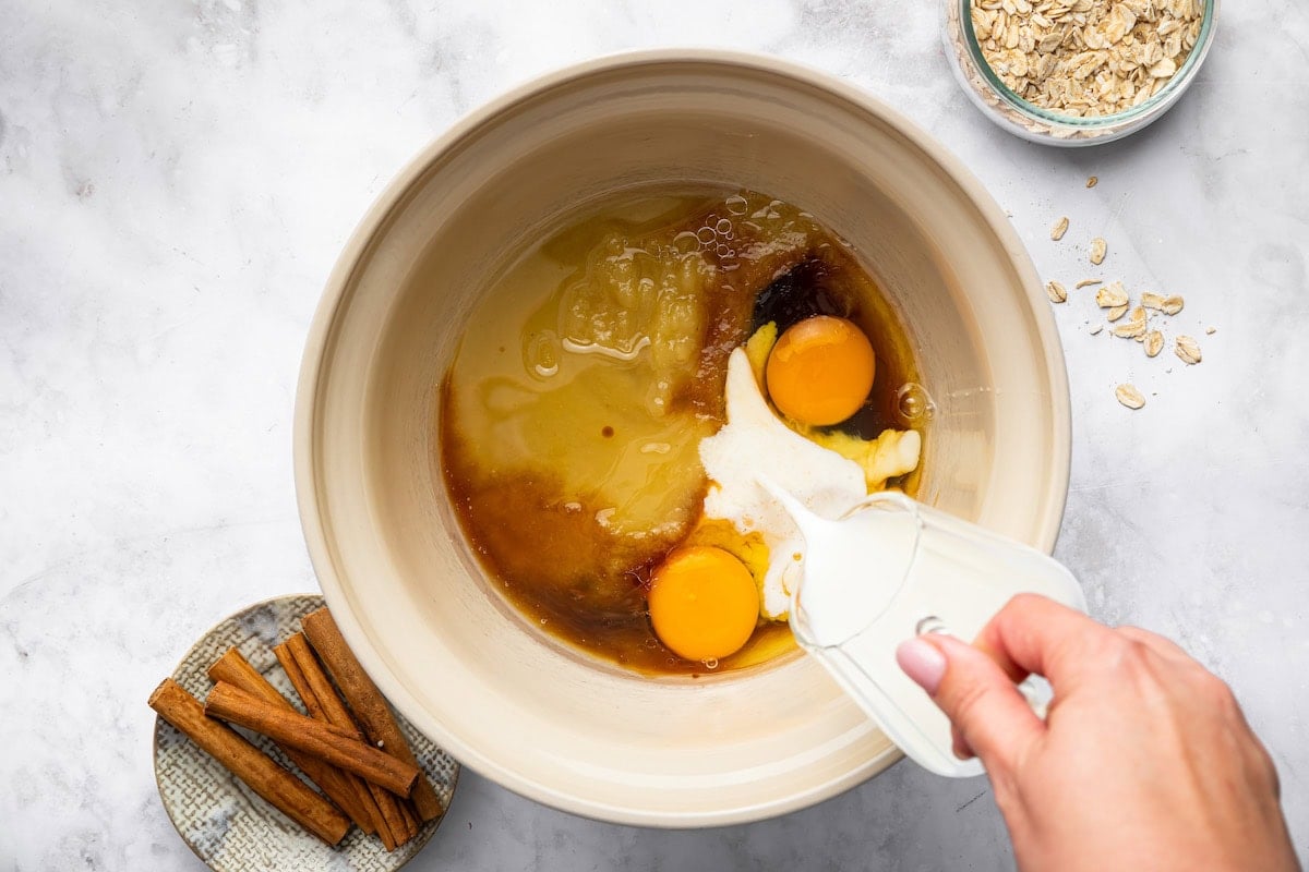 Pouring applesauce, eggs, and maple syrup into the mixing bowl.