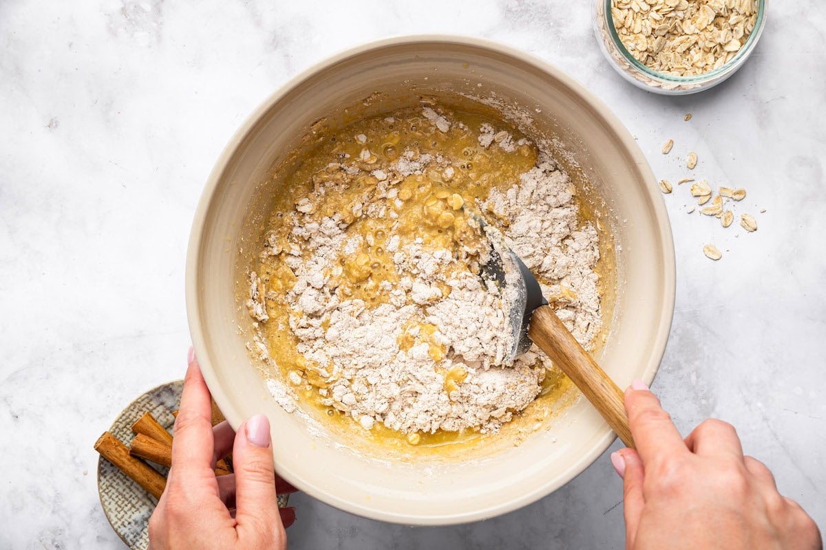 Mixing wet ingredients for applesauce muffins in a beige mixing bowl.