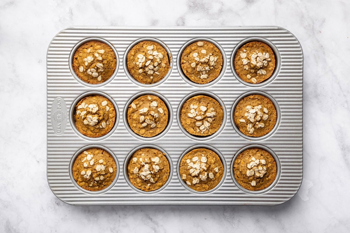 Baked applesauce muffins in a muffin tin, topped with oats and fresh from the oven.
