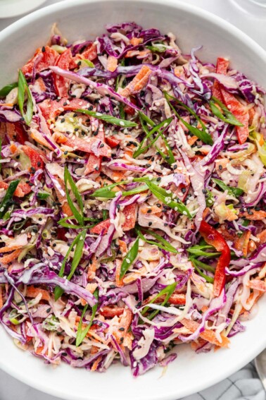 Asian slaw, highlighting the texture and color of the shredded vegetables, garnished with sliced scallions and sesame seeds.