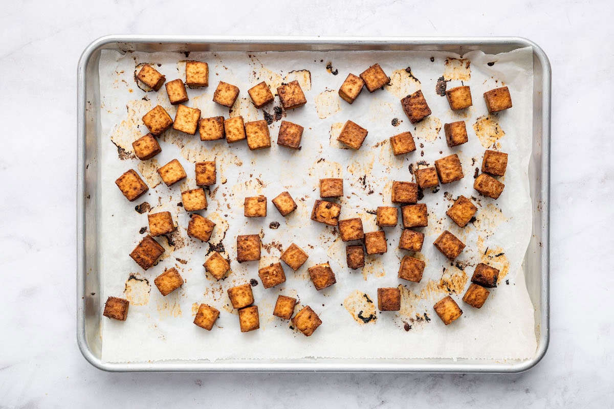 Golden, crispy tofu cubes baked on a parchment-lined sheet pan.