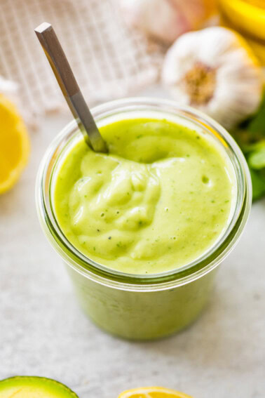 Glass jar filled with avocado dressing, garnished with parsley, lemon, and garlic in the background.