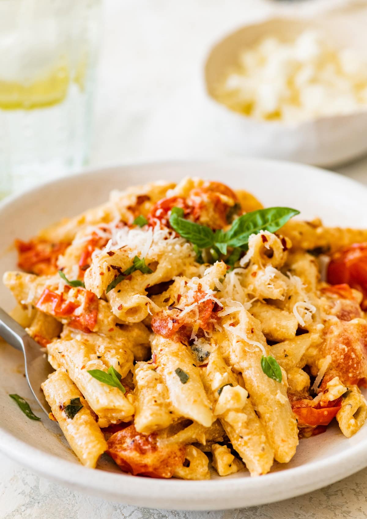 Baked feta pasta on a white plate with basil and parmesan sprinkled on top.