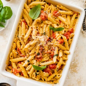 Baked feta pasta in a white baking dish topped with basil and grated parmesan.