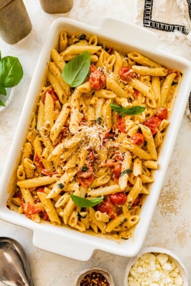 Baked feta pasta in a white baking dish topped with basil and grated parmesan.