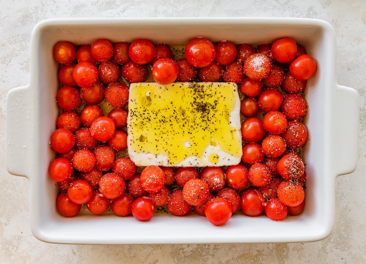 Baking dish filled with cherry tomatoes and a block of feta drizzled with olive oil and sprinkled with salt and pepper before baking.