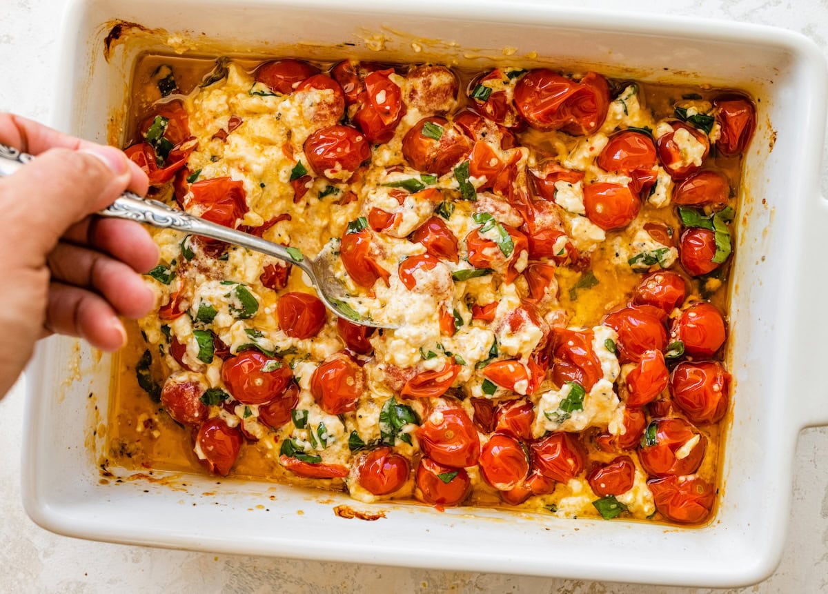 Baked feta and roasted cherry tomatoes in a dish, ready to be stirred together.