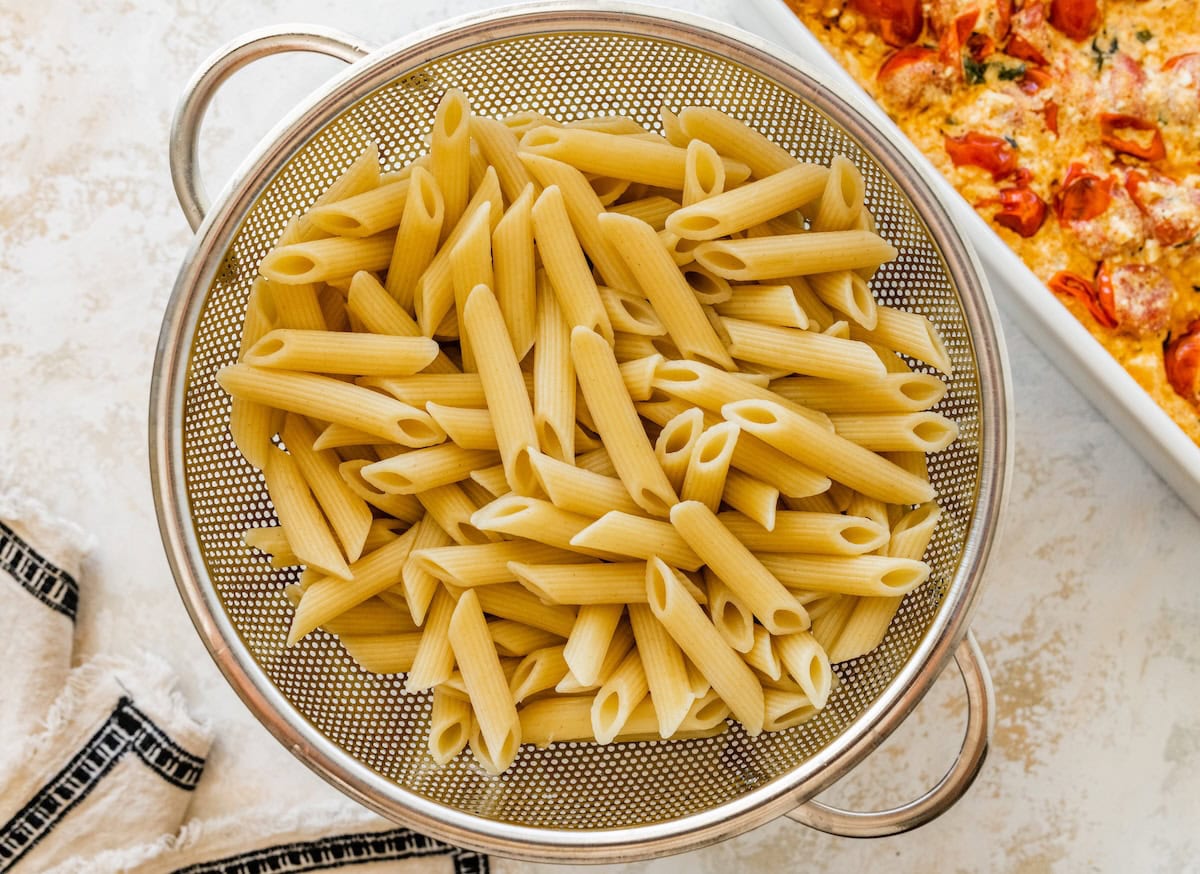 Cooked penne pasta in a metal strainer.