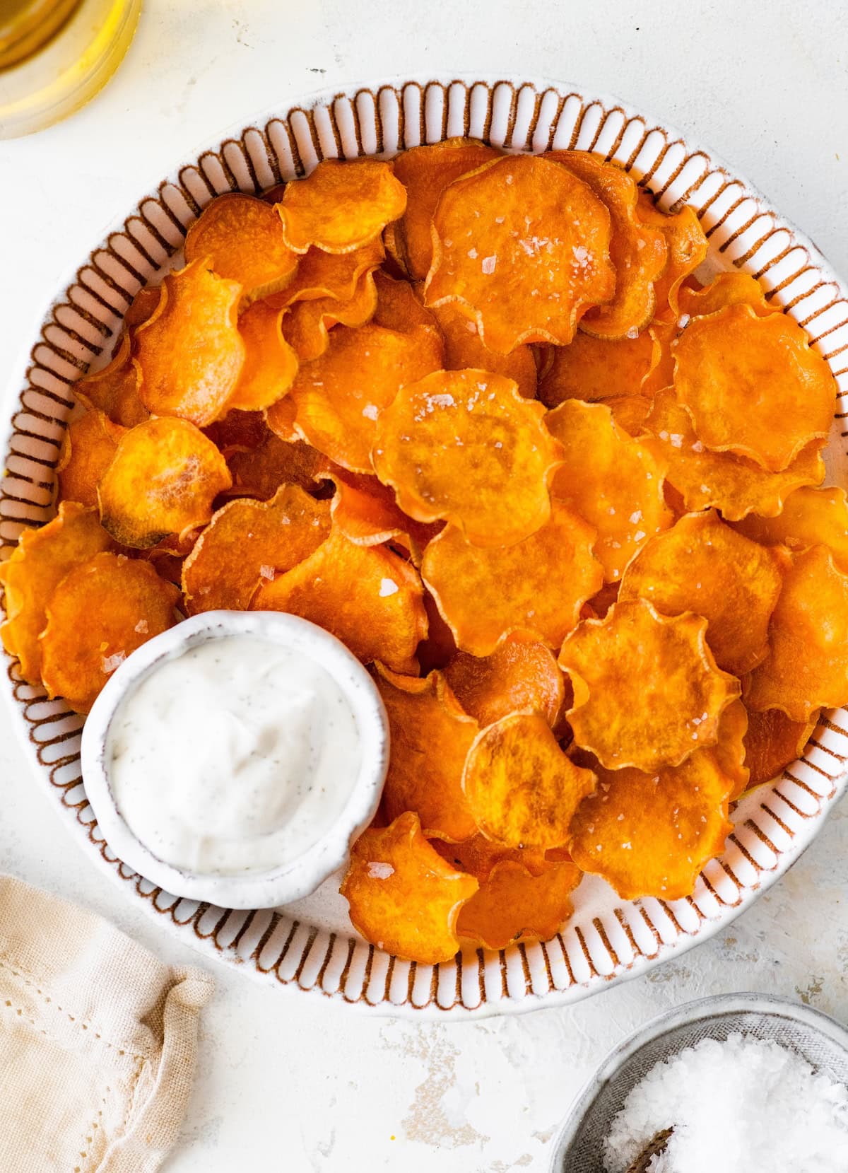 Homemade baked sweet potato chips served in a striped bowl with a side of dip.