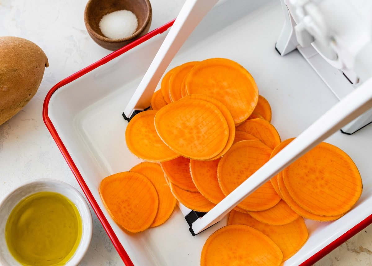 Sweet potato chips being cut by a mandoline slicer.