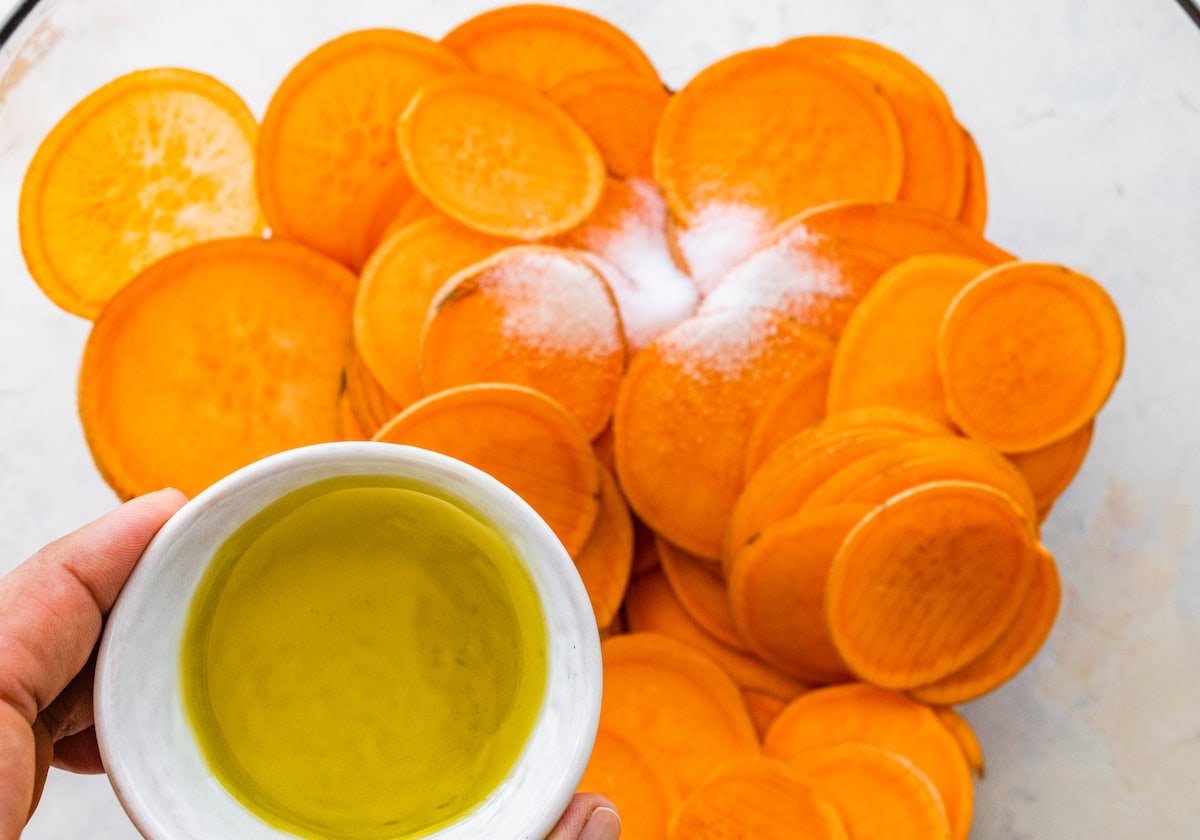 Sweet potato slices sprinkled with salt. Olive oil is being poured onto the sweet potato slices.