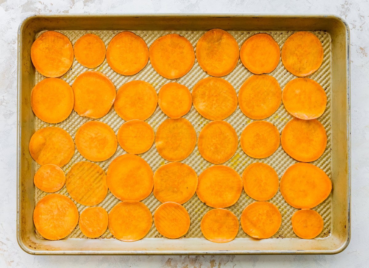 Raw sliced sweet potatoes arranged on a baking tray ready to bake.