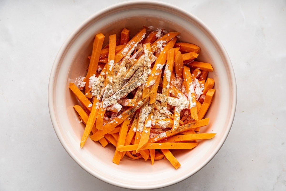Sweet potato fries in a large bowl with seasonings.