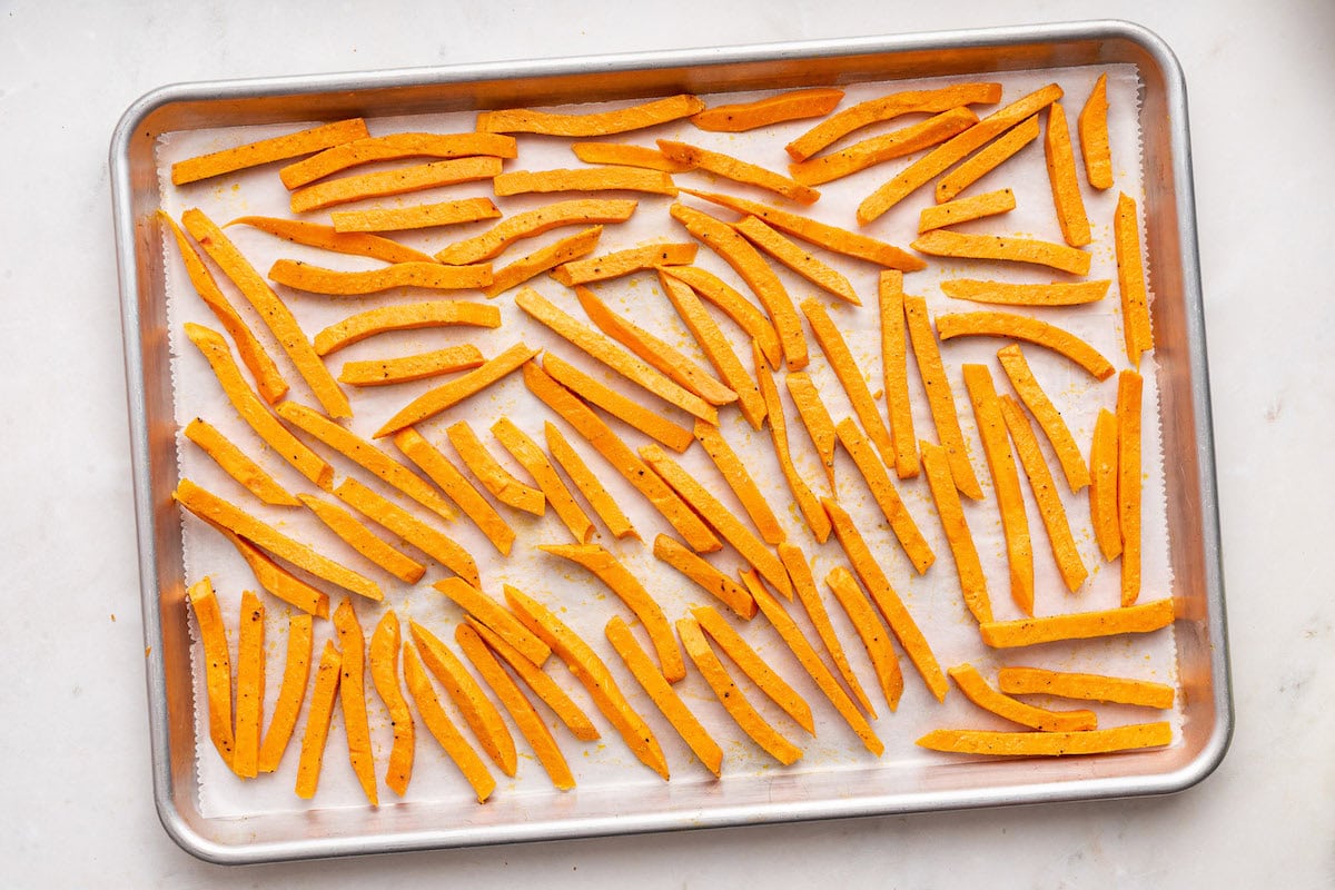 Sweet potato fries spread out on a baking tray before being baked.